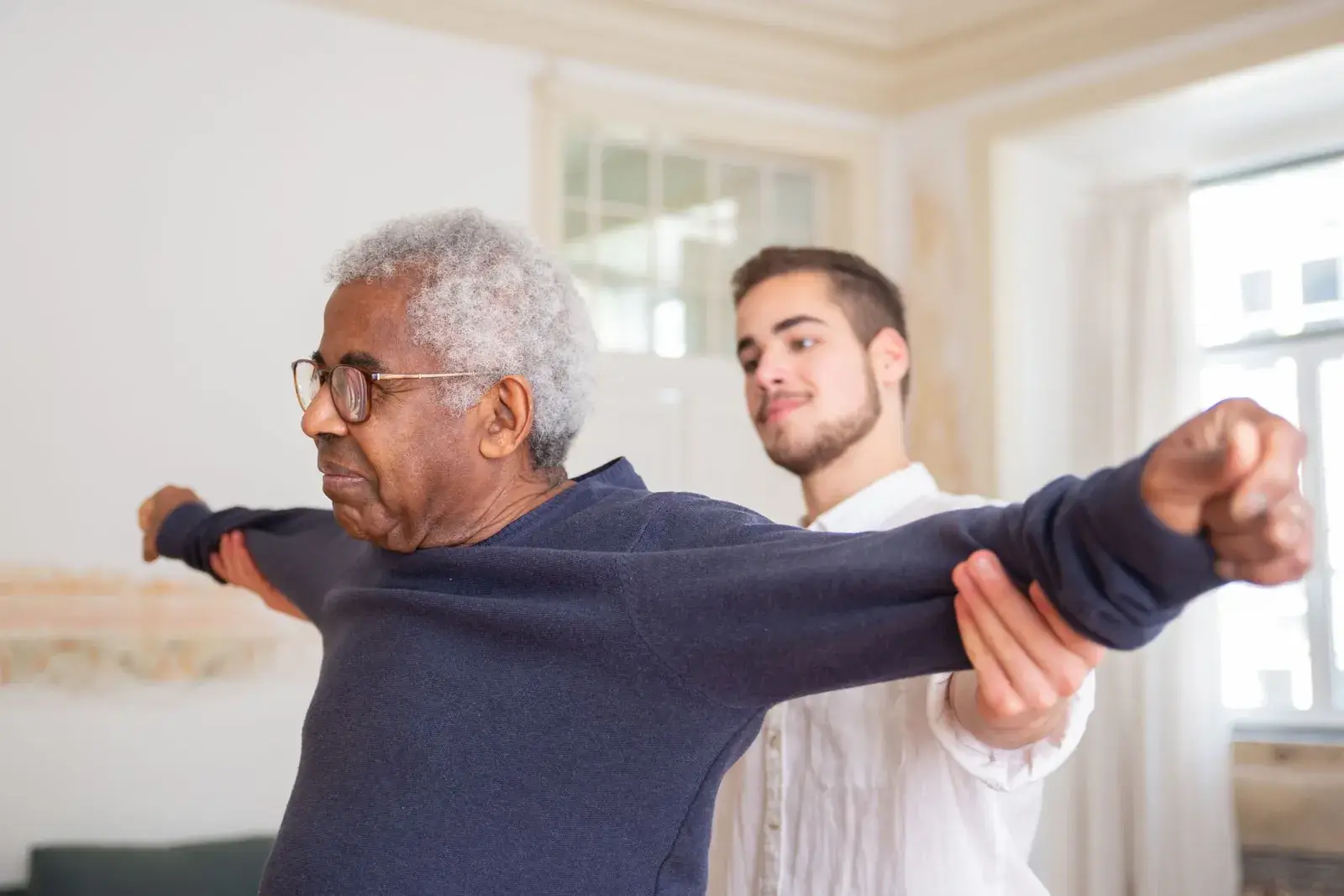 A therapist steadying an older man as he holds his arms out during a balance assessment